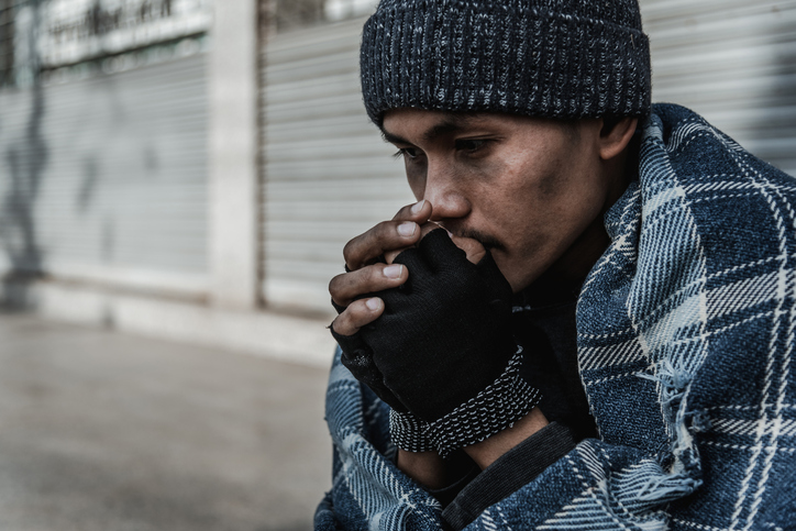 person experiencing homelessness blowing on hands to keep warm