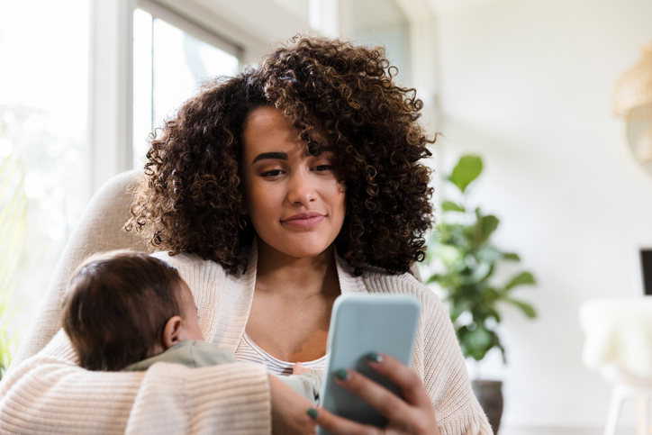 New mom with child uses smartphone at home