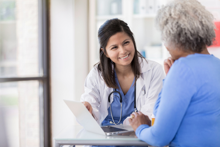 Young nurse uses laptop while sitting with senior patient