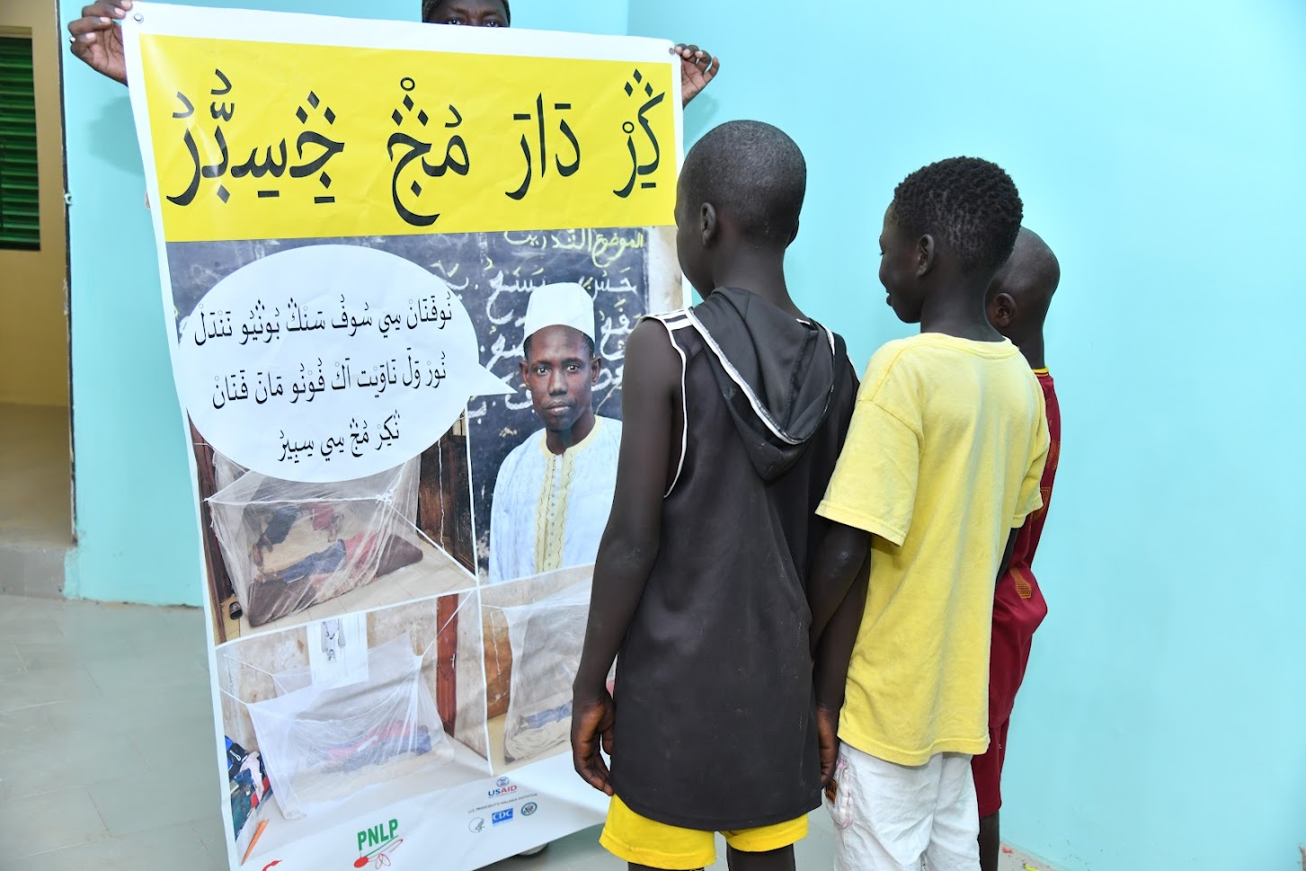 Talibé children in front of the poster in Wolof written in Arabic. Photo Credit: Louis Dasylva, photographer