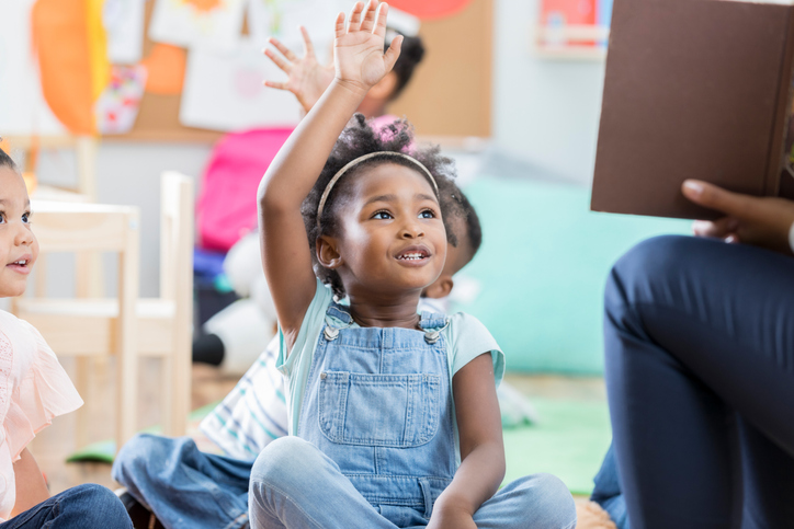 little girl raising her hand in classroom