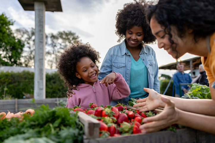 Vibrant Neighborhoods: A Key to Transforming Community Health & Driving Economic Growth. Image description: Happy girl shopping at the Farmer's Market with her mother