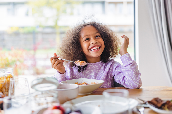 Implementing Summer EBT: Key Considerations - image description: Adorable Girl With Curly Hair Smiling While Eating Breakfast In A Bright Kitchen