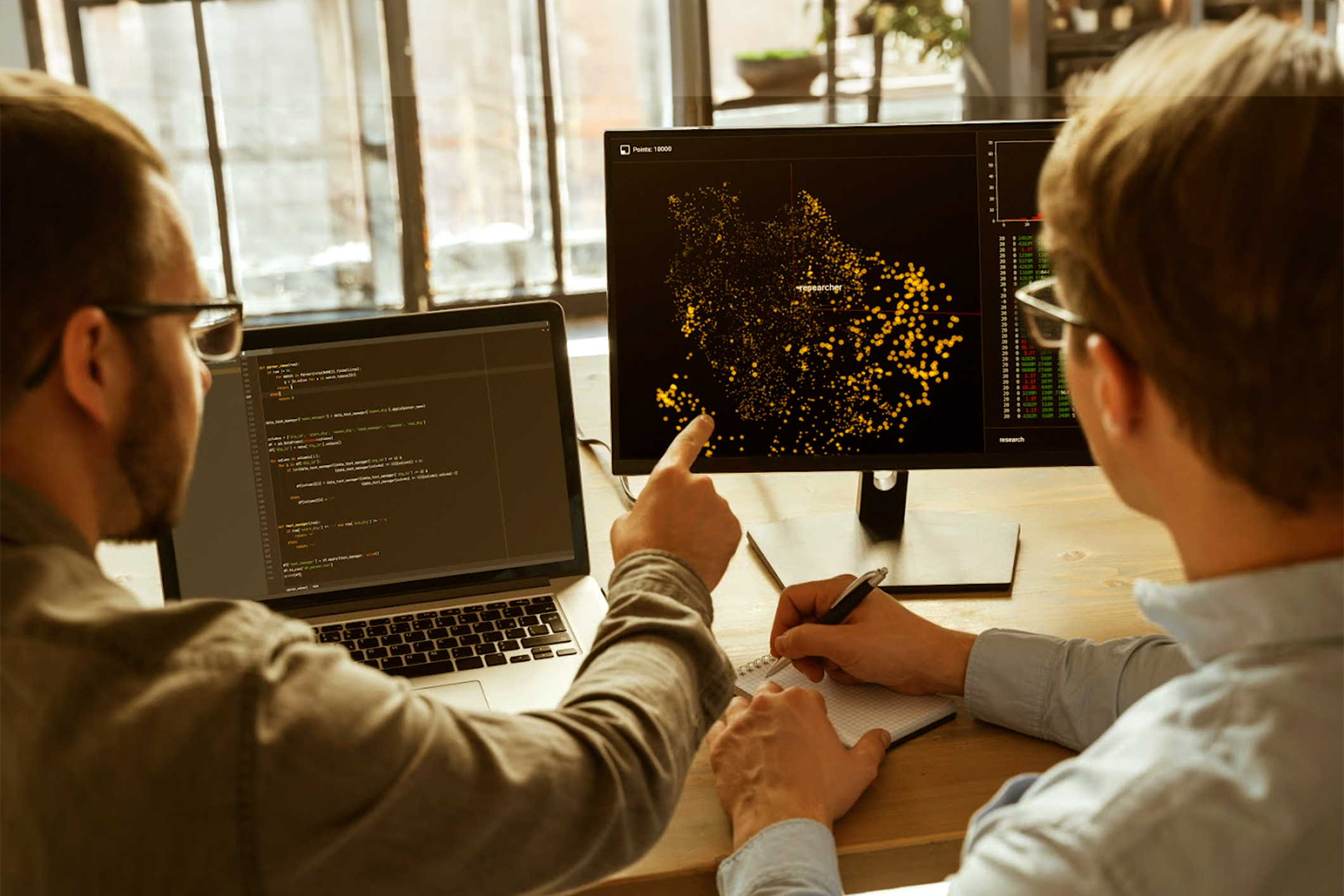 Man pointing to data on a computer screen with another man