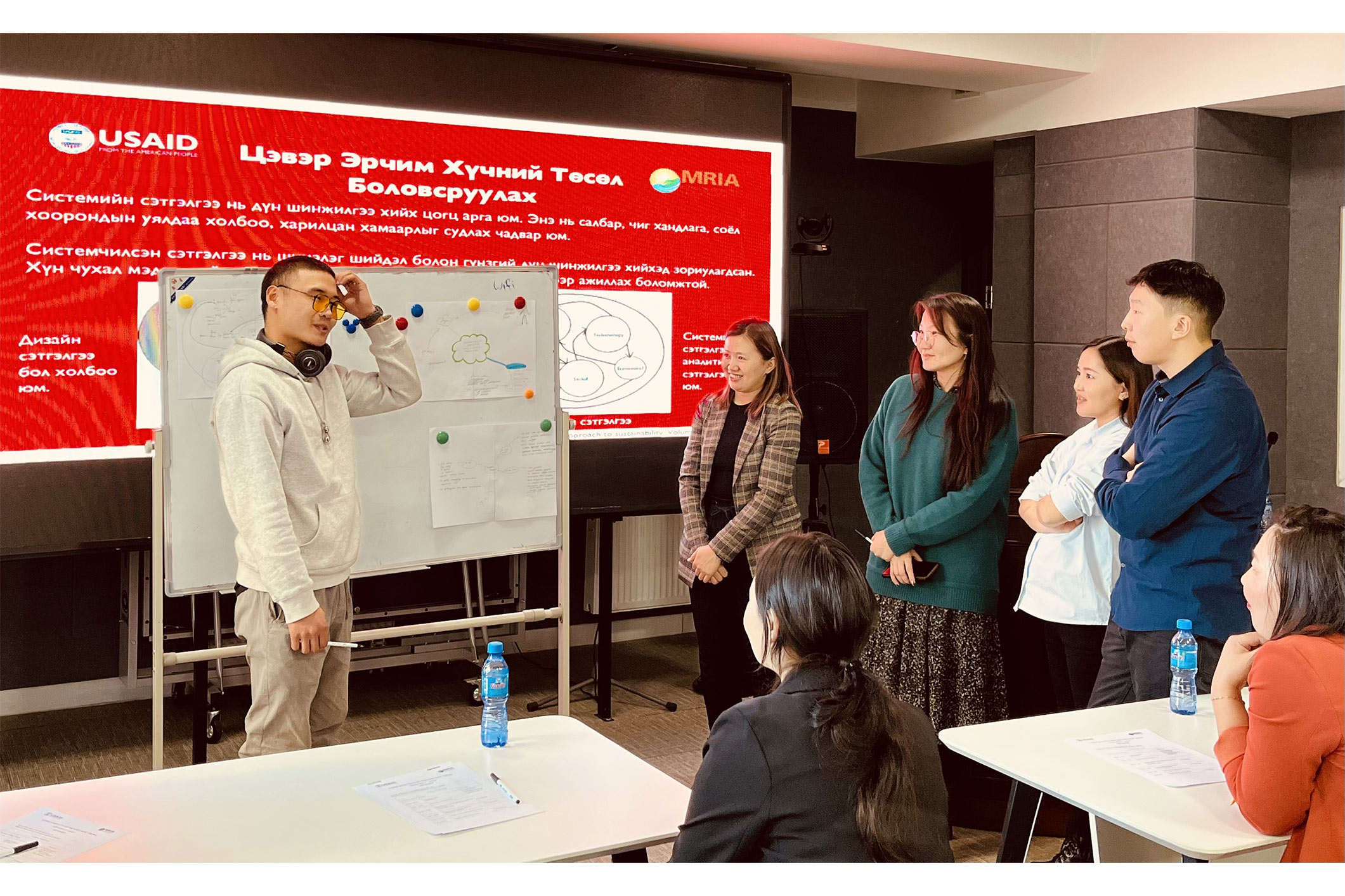 Young Asian man standing in front of white board speaking in front of group of Asian adults