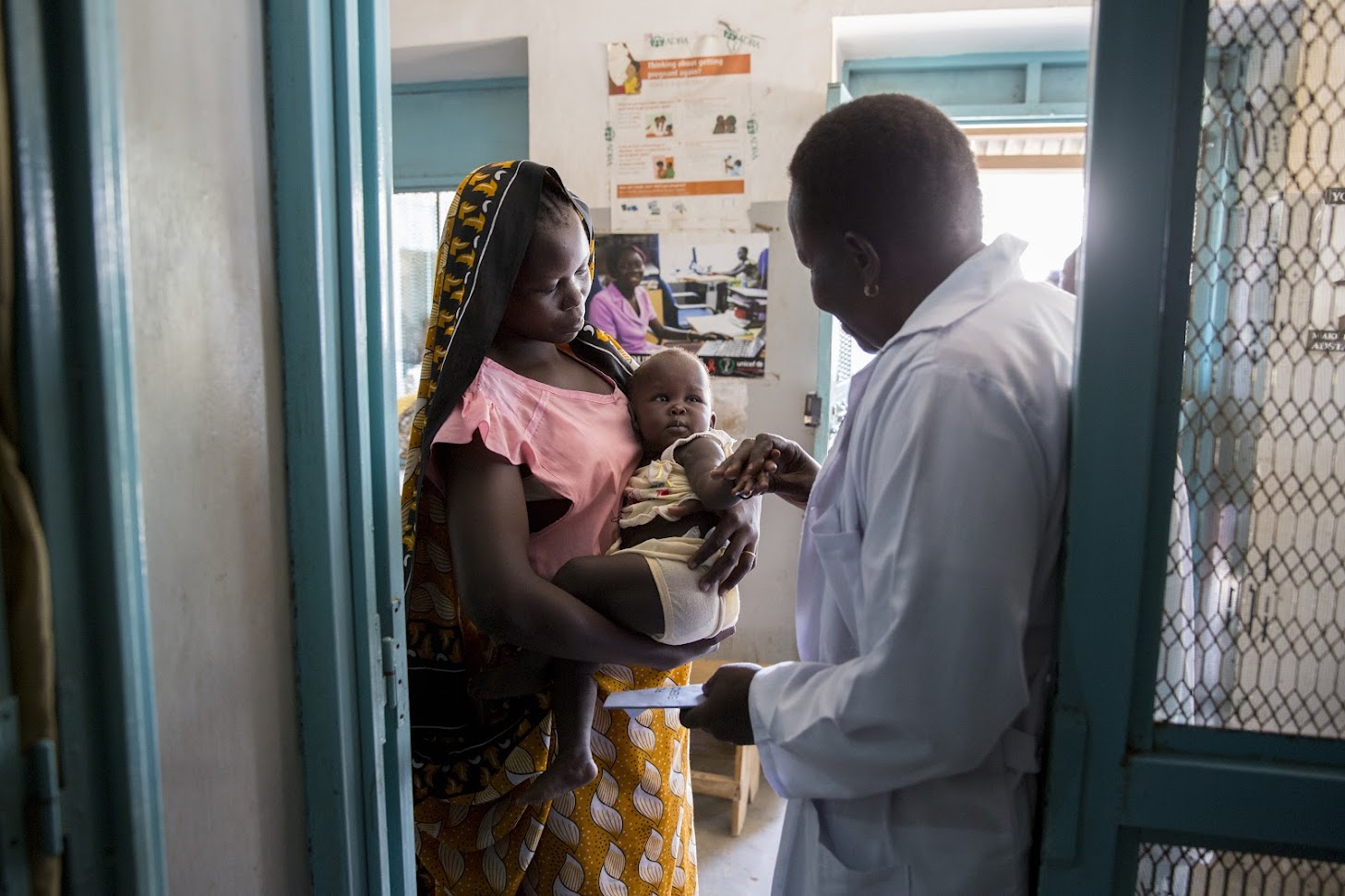 African doctor at a clinic playfully holding the foot of a baby being held in her mother's arms
