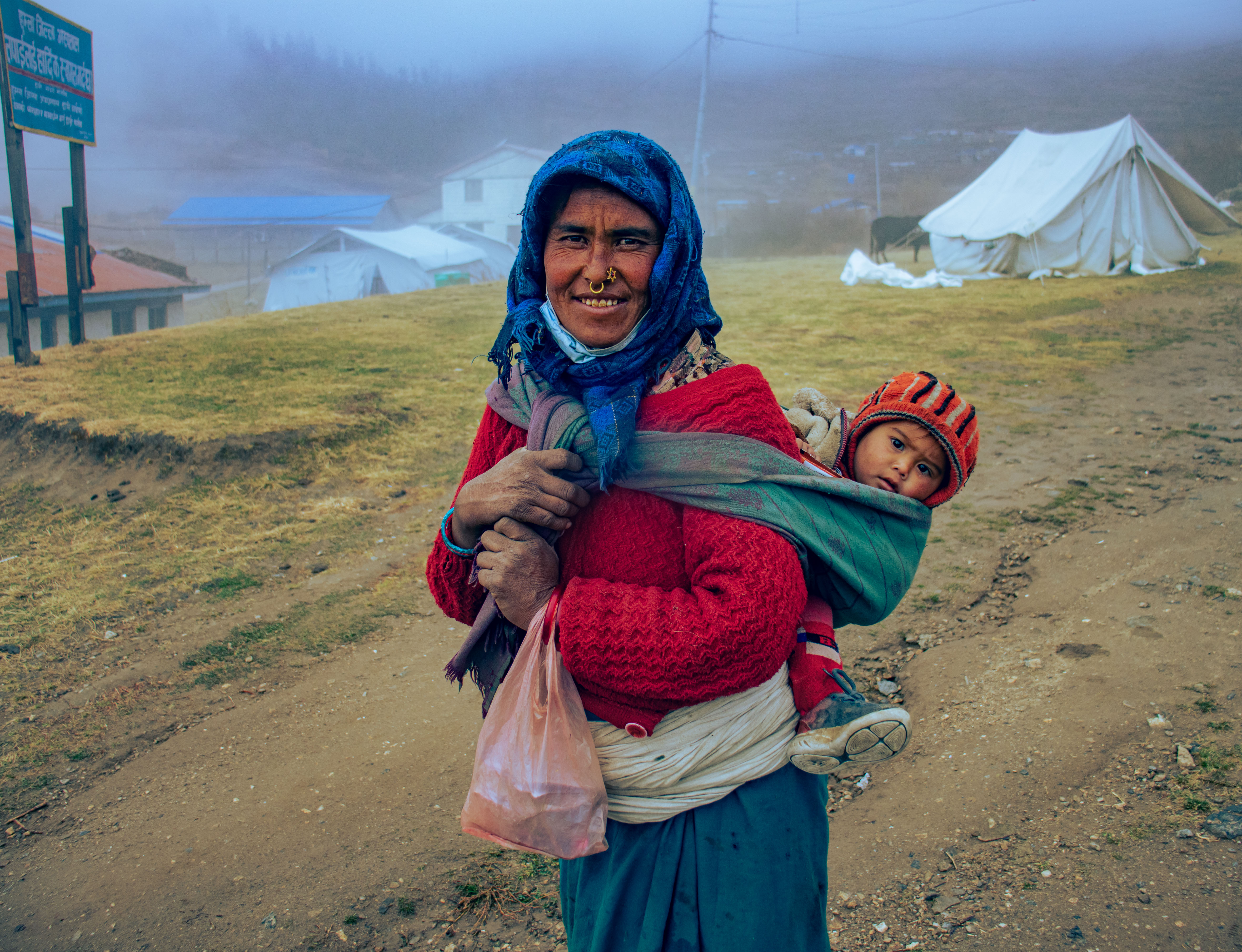 Nepalese mother smiing outside with her infant in a wrap on her back