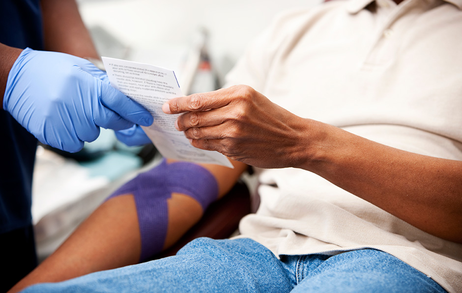 patient having his blood drawn looking at info being handed to him by a nurse