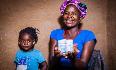 woman in africa holding HIV medicine and smiling next to her daughter