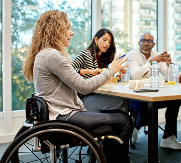 Women in a wheelchair at a conference table, talking to her colleagues.