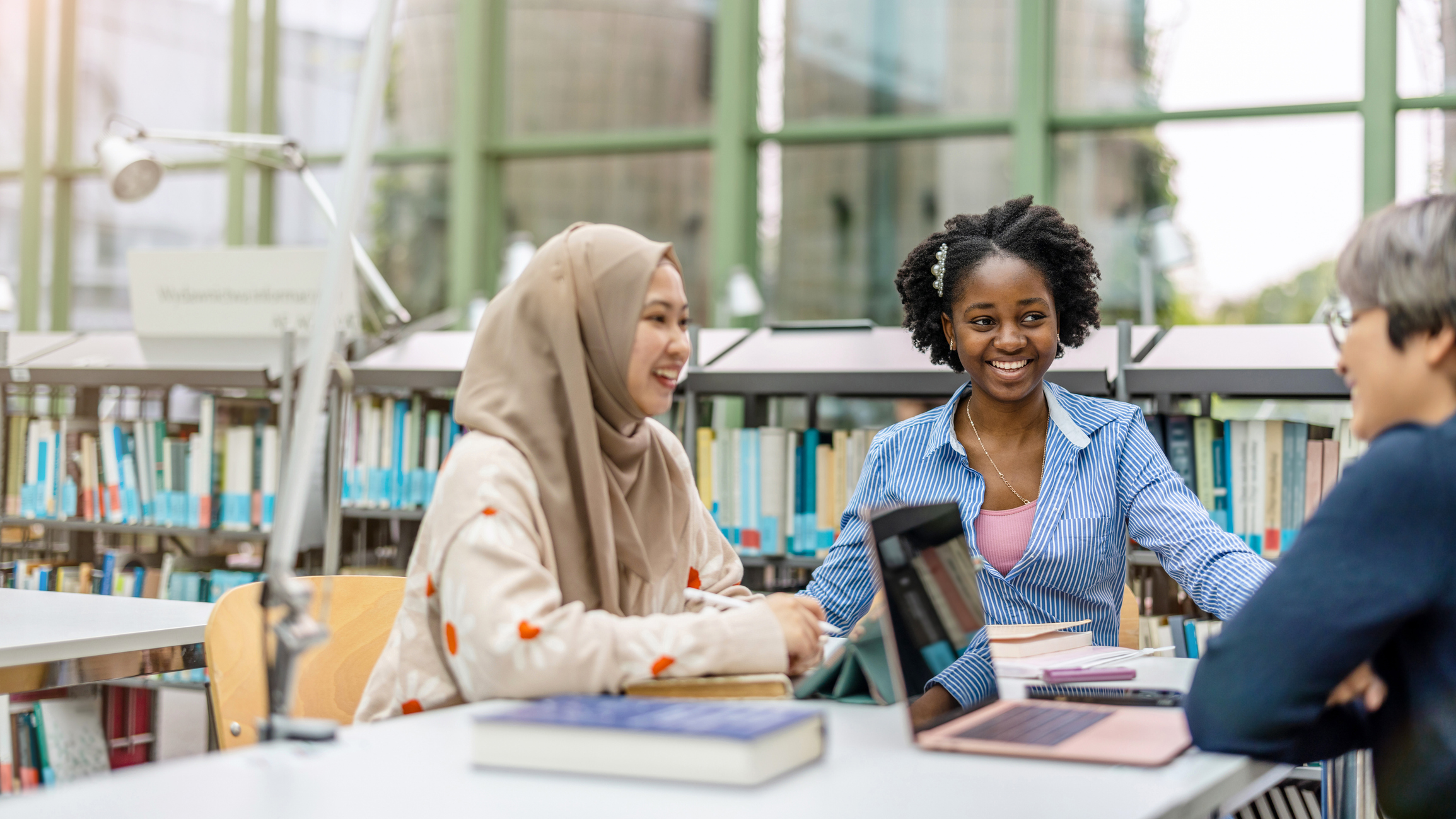 three post graduate women students talking in a library