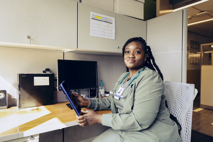 Portrait of smiling female nurse sitting at desk with tablet PC