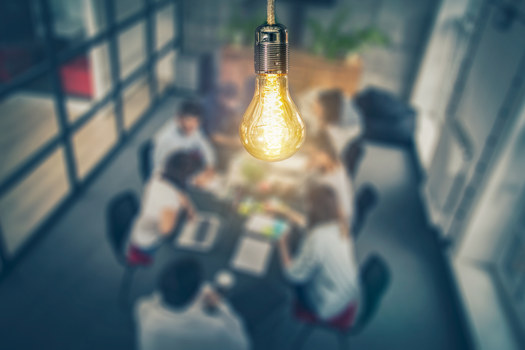 artistic image of a lit lightbulb with people around a conference table in the background