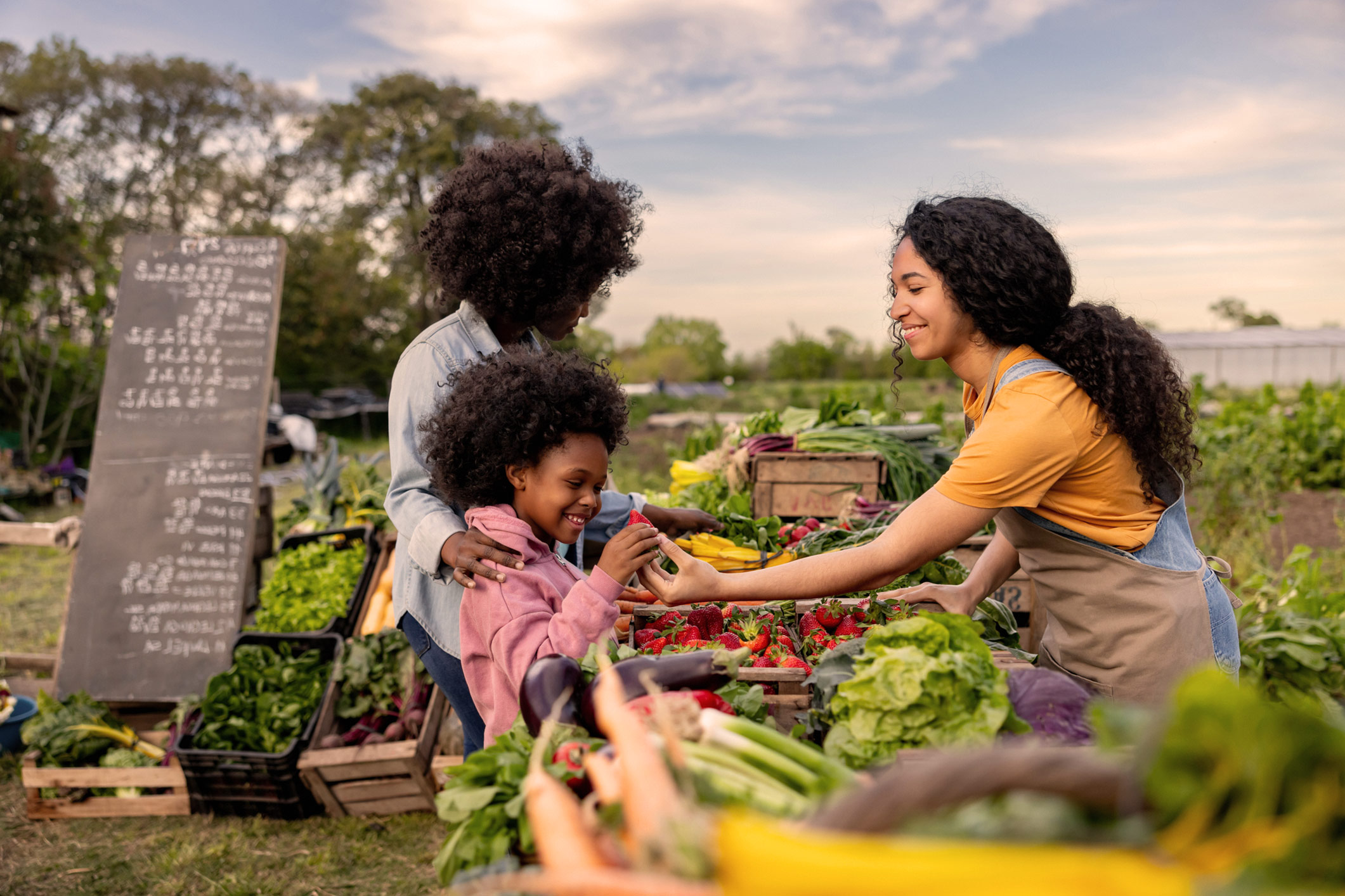 woman handing a young girl a strawberry at an outdoor farmer's market