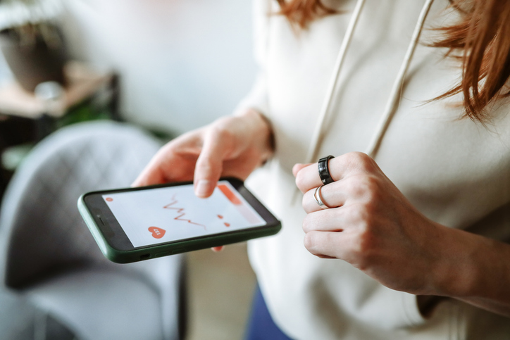 Woman in a hoodie with a smart ring checks heart rate on her phone app