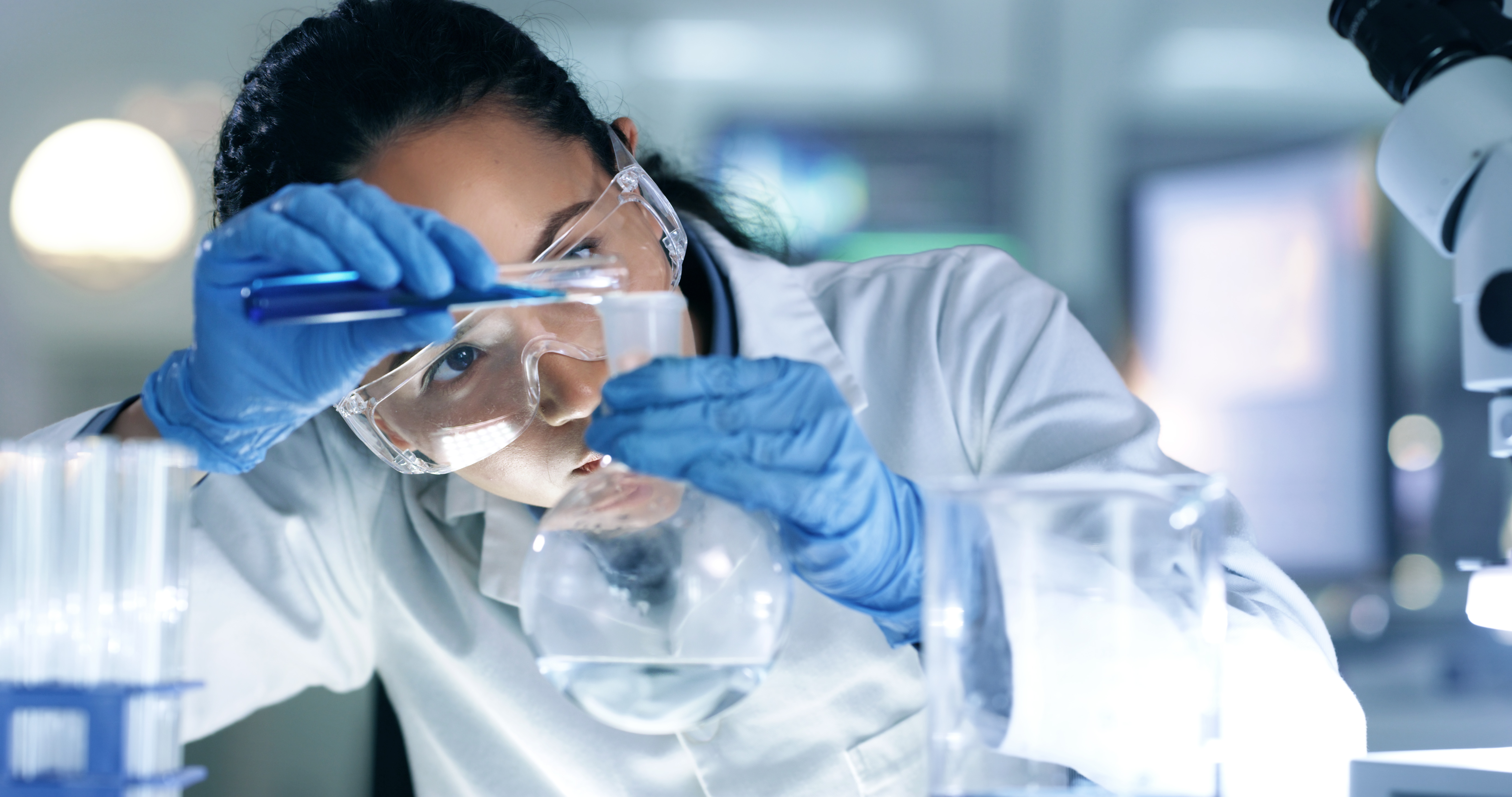 woman scientist looking closely as she pours a liquid into a beaker