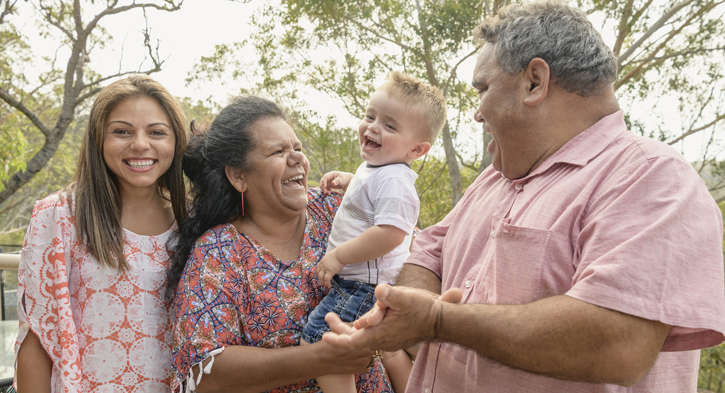 Portrait of three generation Aboriginal family - Grandparents holding little boy, mother smiling towards camera, grandfather clapping