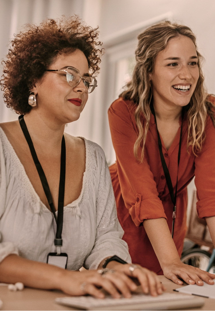 Two women review content on a computer monitor.