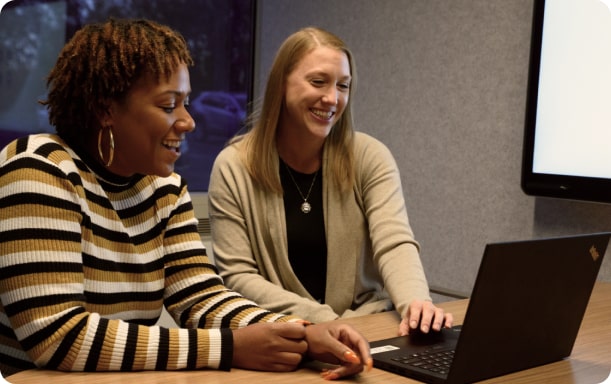 Two women colleagues smiling as they review information together from a laptop.