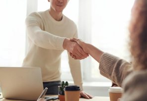 man standing, reaching across a desk to shake a woman's hand