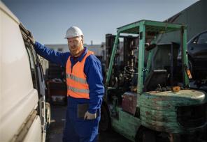 worker in orange vest and hard hat next to forklift