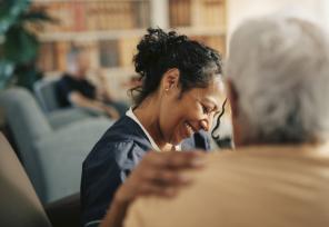 Smiling female nursing assistant with hand on shoulder of senior patient at retirement home