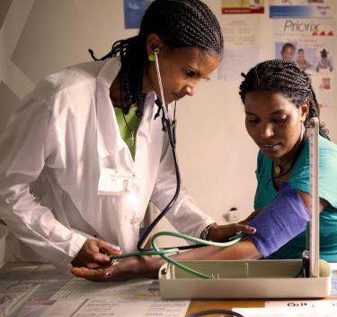 Woman doctor with stethoscope in ears listening to a patient’s pulse under a blood pressure cuff.
