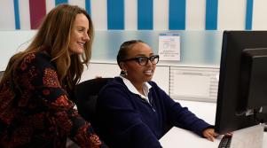Two women colleagues smiling as they review information together on a computer.