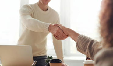 man standing, reaching across a desk to shake a woman's hand