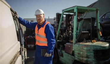 worker in orange vest and hard hat next to forklift