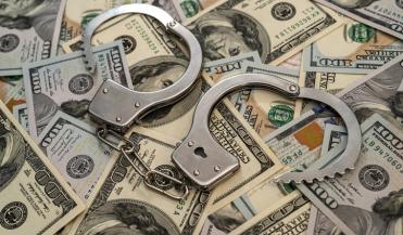 artistic image of handcuffs lying on top of a pile of 100 dollar bills