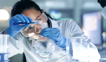 woman scientist looking closely as she pours a liquid into a beaker