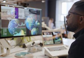 Man looking at a computer monitor showing images of globes and charts of data.