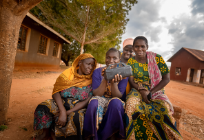 group of women in tanzania smiling and listening to a portable radio