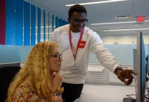 abt employee pointing to computer screen to colleague sitting at desk