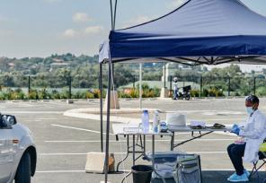 car pulling up to outdoor vaccine tent in a parking lot with clinicians