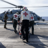 Navy medical crew rushing stretcher across aircraft carrier deck to a helicopter