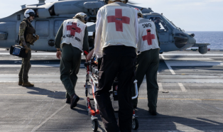 Navy medical crew rushing stretcher across aircraft carrier deck to a helicopter